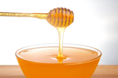 Altın ballı şelaleler, ahşap bir çanaktan temiz bir kaseye dökülüyor ve zengin, yapışkan dokusunu sergiliyor. Bu doğal tatlandırıcı içeceklere ve hamur işlerine tat katmak için idealdir..