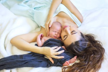 Bir anne, yeni doğmuş bebeğini kucaklarken şefkatle ona bakar. Yumuşak battaniye ve huzurlu atmosfer anneliğin ilk saatlerinde aralarında huzurlu bir an yaratıyor..