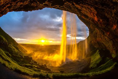 Seljalandsfoss 'un düşen sularından geçen altın güneş ışığı İzlanda' da nefes kesici bir manzara yaratıyor..