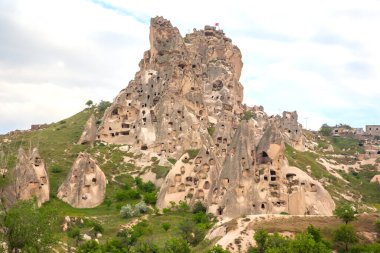 Türkiye 'nin başkenti Kapadokya' da nefes kesici kaya oluşumları görkemli bir şekilde yükseliyor ve taşın üzerine oyulmuş antik mağara evleri sergileniyor. Yeşillik yemyeşil bulutlu bir gökyüzünün altında eşsiz bir manzarayı kaplar..