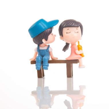 İki minyatür figür, bir oğlan ve bir kız, küçük bir bankta oturuyorlar. Kız dondurmanın tadını çıkarırken oğlan mavi bir şapka ve tulum giyer. Neşeli etkileşimleri neşeli bir anı yakalar..