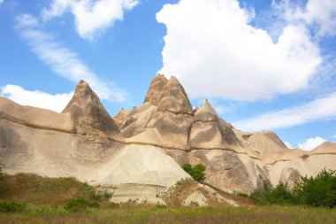 Türkiye 'nin Kapadokya bölgesinde eşsiz jeolojik oluşumlar görkemli bir şekilde yükseliyor ve dağınık bulutlu canlı mavi gökyüzüne karşı belirgin şekillerini sergiliyorlar..