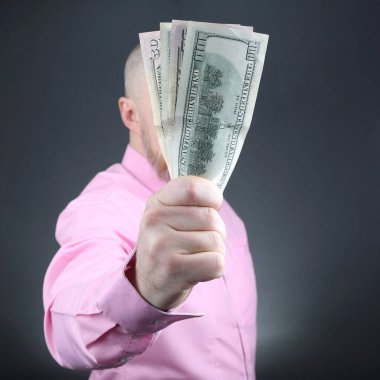 Bir insan gururla arka planda durur. Elinde bir avuç dolusu parayla düğmeli pembe bir gömlek giyer..