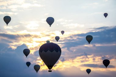 Güneş Türkiye üzerinde yükselirken, gökyüzünde zarif bir şekilde yüzen renkli sıcak hava balonları güzel bir manzara yaratıyor. Sahne, sabahın erken saatlerinde bir sükunet ve macera anı yakalar..