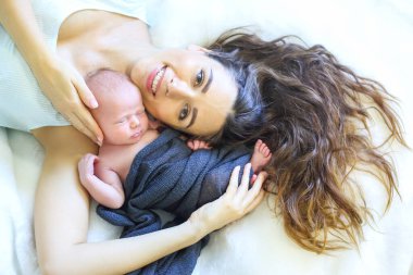 Bir anne yeni doğmuş bebeğini rahat bir ortamda kucaklıyor ve bağlarını parlaklaştırıyor. Yumuşak battaniye, huzurlu atmosfere sıcaklık katar. Huzurlu bir aşk ve şefkat anı yakalar..