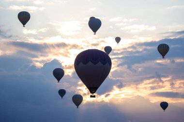 Renkli sıcak hava balonları, şafağın yumuşak ışığıyla aydınlanan gökyüzünde usulca süzülür..