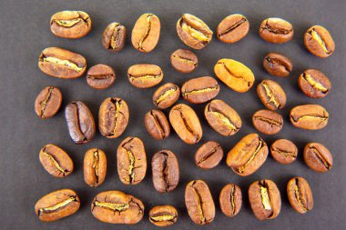 Koyu bir yüzeye serpilmiş taze kavrulmuş kahve çekirdekleri zengin renkler ve dokular sergiliyor..