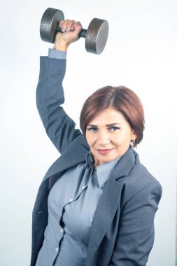 İş elbisesi giymiş bir kadın halterini kendine güvenerek kaldırır, gücünü ve kararlılığını gösterir. Bu kapalı etkinlik profesyonellik ve kişisel uygunluk dengesini vurgular..