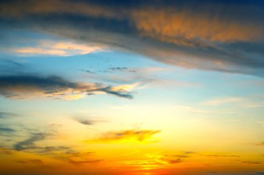 Göz kamaştırıcı bir gün batımı canlı portakallar ve sarılar mavi gökyüzüne karışırken ince bulutlar da akşam sakin bir manzaranın üzerinde büyüleyici bir görüntü oluşturur..
