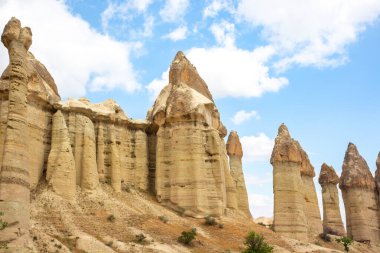 Ziyaretçiler, Türkiye 'nin Kapadokya kentindeki manzaradan yükselen çarpıcı peri bacalarına hayran. Kaya oluşumları yüzyıllar boyunca doğa tarafından oyulmuş karmaşık şekiller sergiliyor..