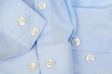 Açık mavi gömlek kumaşı sergileniyor, beyaz düğmeler ve karmaşık dikişler sergileniyor. Yapısı ve işçiliği elbisenin kalitesini ve tarzını vurguluyor ve görsel olarak çekici kılıyor..