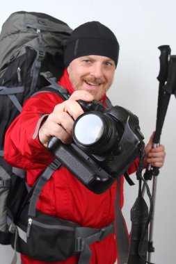 Parlak kırmızı ceket giymiş bir kişi, büyük bir sırt çantası ile kamerayı elinde tutarak güvenle ayakta duruyor. Bu ayar, soğuk hava koşullarında açık hava keşiflerine odaklanmayı gerektiriyor..