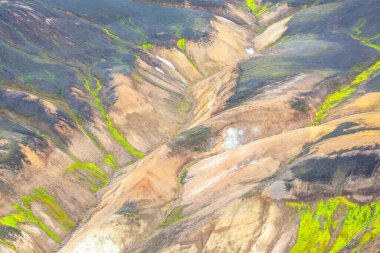 İzlanda 'nın dağlık bölgelerinin renkli tepeleri ve vadileri yemyeşil alanlara karşı çarpıcı bir görsel zıtlık yaratır. Jeotermal aktivite araziyi şekillendirir, canlı renkler ve dokular ortaya çıkarır..