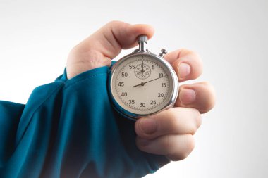 A hand grips a classic stopwatch, showcasing the time in a quiet indoor environment. The focus emphasizes the stopwatch's intricate details and the person's intent on timing an activity.