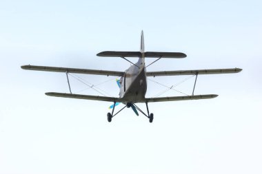 A biplane soars above the landscape on a sunny afternoon, showcasing its vintage design against a backdrop of blue skies and soft clouds. The flight highlights aviation and nostalgic transport.