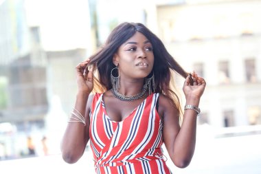 Bir Afrikalı kadın şehir ortamında, saçlarıyla oynarken kendine güvenini sergiliyor..
