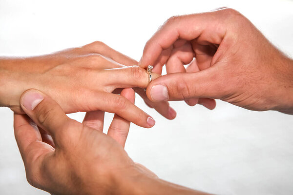 Две руки, занимающиеся в нежный момент, как кольцо помещается на палец, символизируя любовь и преданность. Яркий фон подчеркивает важность этого интимного случая.