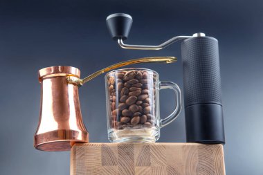 Parlak bakır bir kahve seti, bir bardak kavrulmuş kahve çekirdeği, ve ince bir manuel öğütücü, ahşap üzerine koyu arkaplan ile zarif bir şekilde düzenlenmiş.