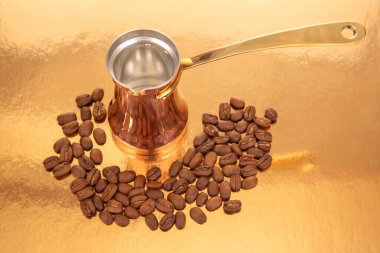 Kahve çekirdeğinin yanında altın saplı geleneksel bakır çakmak. Lüks altın bir yüzeye kurulmuş. Gurme kahve ve mutfak dekorları için ideal.