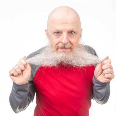 Uzun beyaz sakallı kel yaşlı bir adam sakalını iki eliyle çekiyor, kırmızı ve gri atletik bir gömlek giyiyor, beyaz bir arka planda izole edilmiş, komik bir ifade sergiliyor.