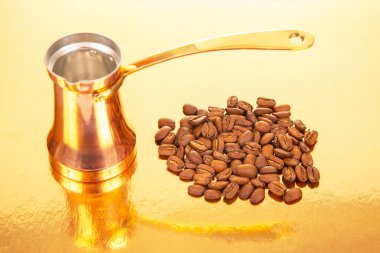 Altın bir arka planda, kahve kültürü ve içecek teması için mükemmel olan kavrulmuş kahve çekirdekleri yanında pirinç saplı parlak bir bakır Türk kahve demliği.