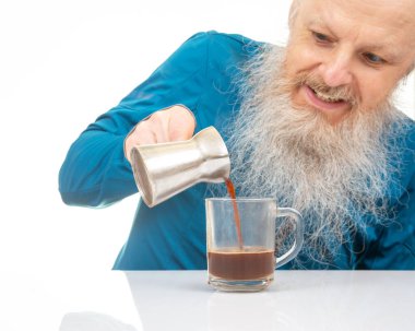 Uzun beyaz sakallı mutlu bir adam ev yapımı kahvaltı atmosferinde beyaz bir bardağa kahve dolduruyor. sıcak içecek.