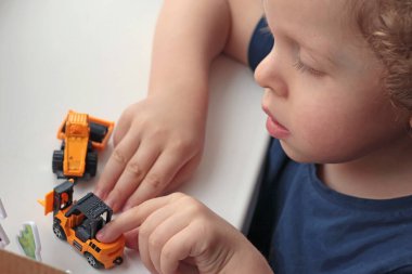 Beyaz masada arabasıyla oynayan kıvırcık saçlı sarışın çocuk. Çocuklar için geliştirme oyunları. - Evet. Yüksek kalite fotoğraf