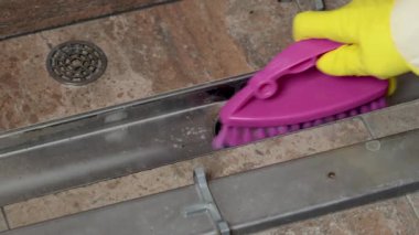 Sarı eldivenli ve pembe fırçalı bir kadın duş kabininde kimyasalları kullanarak giderleri temizliyor. Banyoda temizlik ve düzenlilik var. Temizlik ve düzen. Yüksek kalite 4k görüntü