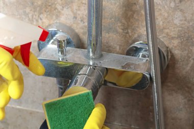 Sarı eldivenli bir kadın banyo musluğunu kimyasal ve süngerle temizliyor. Temizlik ve temizlik. Evle ve düzenle ilgilenmek. Yaşam tarzı. - Evet. Yüksek kalite fotoğraf