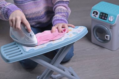 Evde, yerdeki çocuk ütüleme masasında kazak giyen kız. Temizlik, ev işleri, çocuklar ve eğitim oyunları. - Evet. Yüksek kalite fotoğraf