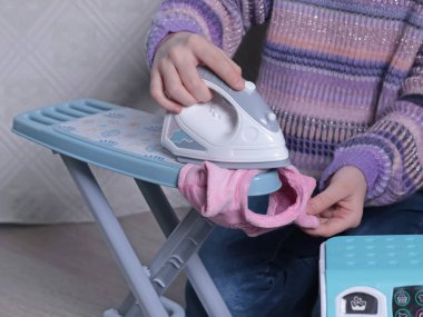 Evde, yerdeki çocuk ütüleme masasında kazak giyen kız. Temizlik, ev işleri, çocuklar ve eğitim oyunları. - Evet. Yüksek kalite fotoğraf