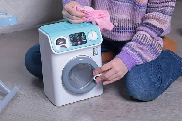 Kız evde yerde oyuncak ütü ve çamaşır makinesiyle oynuyor. Temizlik, ev işleri, çocuklar ve eğitim oyunları. - Evet. Yüksek kalite fotoğraf