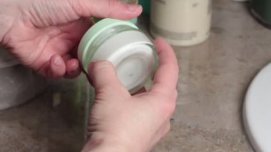 Modern banyoda cam kavanoz krem kapaklı sabahlık giymiş bir kadın. Güzellik ve bakım, spa rutinleri. Yüz besleyici krem. Yüksek kalite 4k görüntü