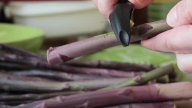 Kadın kabuğu soyar, özel bıçakla mor kuşkonmaz filizleri fırlatır. Diyet ve sağlıklı beslenme. Mevsimlik yiyecekler. - Evet. Yüksek kalite 4k görüntü