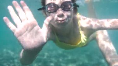 Yüzme gözlüklü kız suyun altında yüzer ve elini sallar. Yazın denizde kutlama ve tatil. Altında çakıl taşları var. Mutluluk ve yaşam tarzı. Yüksek kalite 4k görüntü