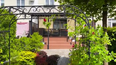 Backyard terrace with polycarbonate canopy. Forged arch with roses. Nature, flowers, plants and summer relaxation. Lifestyle. High quality 4k footage