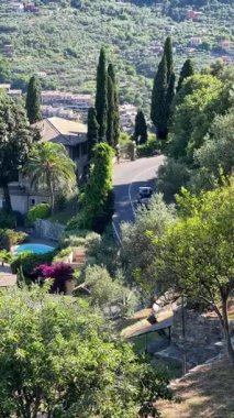 Camogli, İtalya - 11 Temmuz 2025. Araba selvi ağaçları arasında yol boyunca gidiyor. İtalya 'da yaz aylarında turizm. Geleneksel binalar. Tasarım için arka plan. Yüksek kaliteli FullHD görüntüler