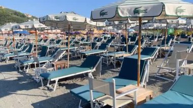 Sestri Levante, İtalya - 9 Ağustos 2025. Deniz kıyısındaki Lacoste markasının plaj şemsiyeleri ve güneş şezlongları. Yazın gün batımı, İtalya, Liguria 'da tatil. Metin için arka plan. Yüksek kalite 4k görüntü