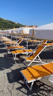 Sestri Levante, İtalya - 9 Ağustos 2025. Plaj şemsiyeleri ve deniz kenarında güneşlenme yerleri. Yazın gün batımı, İtalya, Liguria 'da tatil. Metin için arka plan. Yüksek kalite 4k görüntü