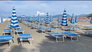 Plaj şemsiyeleri ve deniz kenarında güneşlenme yerleri. Yazın gün doğumu, İtalya, Liguria 'da tatil. Metin için arka plan. Yüksek kalite 4k görüntü