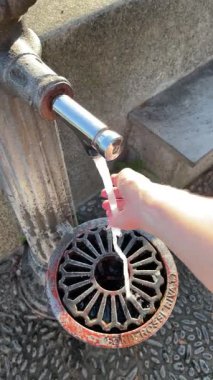 Kadın avucunun içine su topluyor. İtalya 'nın kırsal kesiminde, Avrupa' da, kilisenin yanındaki meydanda su kaynağı. Isı ve küresel ısınma. Geleneksel yapı. Yüksek kalite 4k görüntü