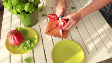 Kadın domatesi seramik bıçakla kesti. Evde sebzeler ve bitkiler var. Çömlekte fesleğen. Sağlıklı beslenme. Çevre dostu ürünler. Akdeniz diyeti. Yüksek kalite 4k görüntü