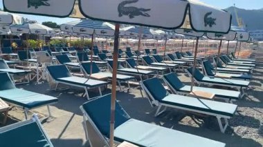Sestri Levante, İtalya - 9 Ağustos 2025. Deniz kıyısındaki Lacoste markasının plaj şemsiyeleri ve güneş şezlongları. Yaz, Liguria, İtalya 'da tatil. Metin için arka plan. Yüksek kalite 4k görüntü