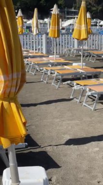 Sestri Levante, İtalya - 30 Ağustos 2025. Plaj şemsiyeleri ve deniz kenarında güneşlenme yerleri. Yaz, Liguria, İtalya 'da tatil. Metin için arka plan. - Evet. Yüksek kalite 4k görüntü