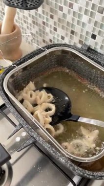 Anonymous person removes rings of sliced, breaded, fried squid from hot frying pan and places them on plate on kitchen counter. Seafood, health, and healthy eating. Traditional food in Italy, organic