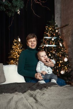 Noel ağacı olan bir yeni yıl mekanında büyükannesiyle birlikte bir çocuk.
