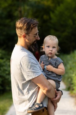 Genç baba ve küçük oğlu güneşli bir günde parkta yürüyorlar.