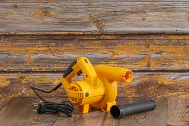 Sarı elektrikli hava üfleyici. Güçlü bir alet olması için uzun bir hortumu var, muhtemelen ahşap yüzeyli enkazı temizlemek ya da temizlemek için kullanılıyor..