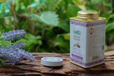 Bangkok, Tayland - Haziran 08, 2024: Yılan Markası Fransız Lavanta kokulu pudra, açık kapaklı konteynır ve açık havada yeşilliklerle çevrili ahşap bir yüzey üzerinde lavanta çiçekleri.