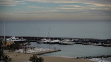 Geniş panoramik bir manzara, gösterişli ve zarif yatlarla süslenmiş hareketli bir İspanyol marinasını gözler önüne seriyor. Yat limanı, tekne meraklıları ve ziyaretçiler gibi enerjik bir enerji yayıyor.